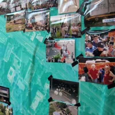 Колаж разних фотографија које приказују протесте и масе залепљен је на тиркизно плаву позадину, са црном траком на сваком углу – истичући уметност, солидарност и активизам унутар визуелне нарације Контекст колектива.